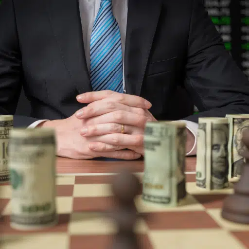 Cash management strategy illustrated by a chess board with rolls of cash as chess pieces and a businessman studying his plan.